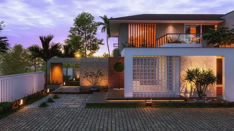 Contemporary tropical-style home elevation in Trivandrum featuring warm lighting, exposed brick textures, breeze blocks, and lush landscape design by Rzian Homez.